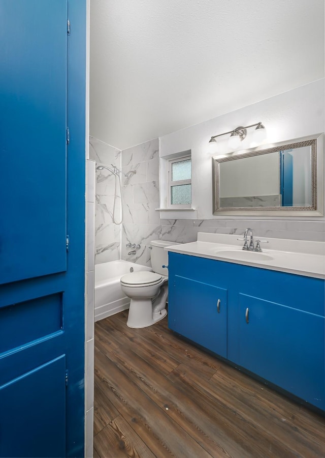 full bathroom featuring toilet, tiled shower / bath, tile walls, vanity, and hardwood / wood-style floors