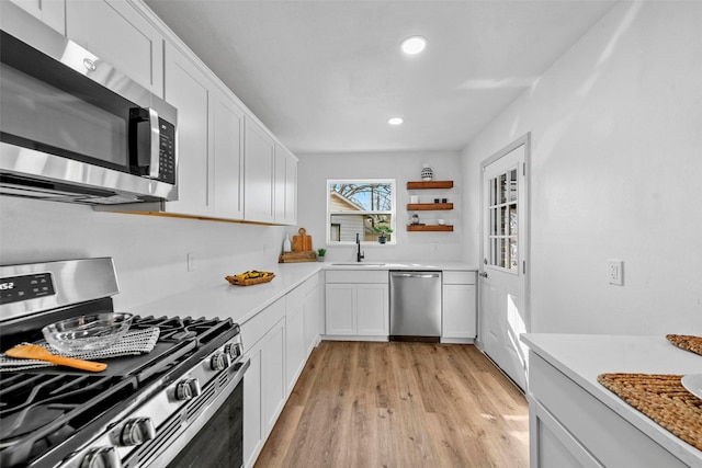 kitchen with appliances with stainless steel finishes, light hardwood / wood-style floors, sink, and white cabinets