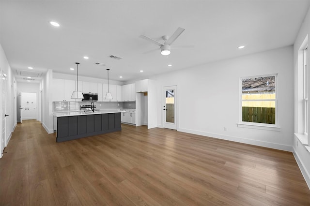 kitchen with sink, decorative light fixtures, hardwood / wood-style floors, a kitchen island with sink, and white cabinets