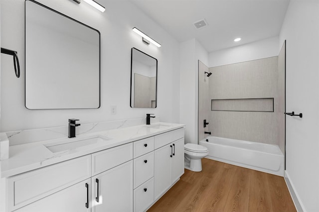 full bathroom featuring hardwood / wood-style flooring, tiled shower / bath, vanity, and toilet