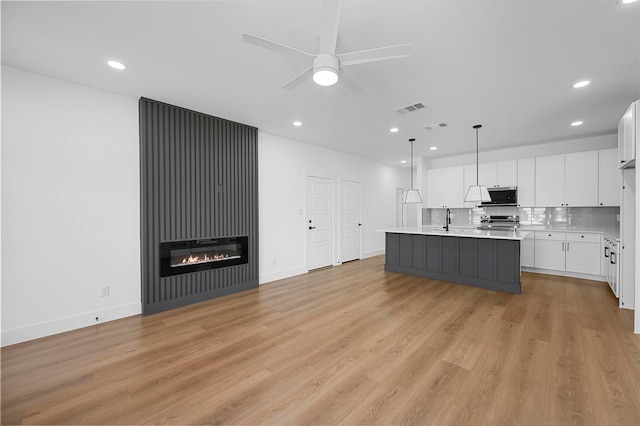 kitchen featuring appliances with stainless steel finishes, decorative light fixtures, an island with sink, sink, and white cabinets