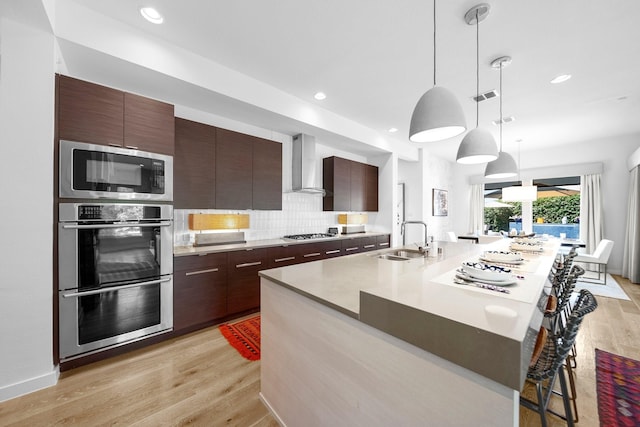 5399 Randwick Trl, Frisco, TX 75036 - kitchen featuring wall chimney range hood, appliances with stainless steel finishes, modern cabinets, a sink, and light wood finished floors