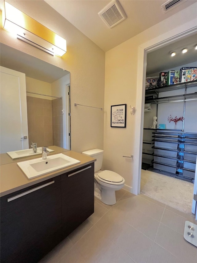 bathroom featuring tiled shower, vanity, toilet, and tile patterned flooring