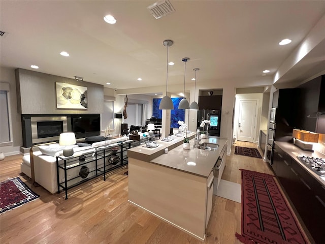 kitchen featuring pendant lighting, stainless steel gas stovetop, sink, a kitchen island with sink, and light hardwood / wood-style floors