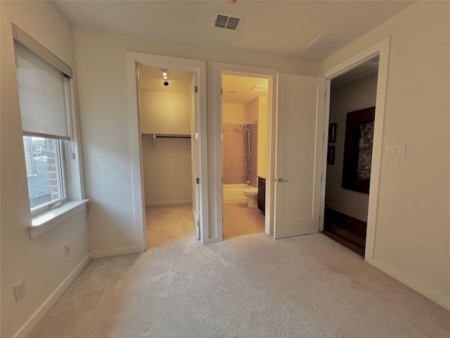 unfurnished bedroom featuring a walk in closet, light carpet, ensuite bath, and a closet