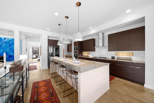 5399 Randwick Trl, Frisco, TX 75036 - kitchen with wall chimney range hood, appliances with stainless steel finishes, modern cabinets, a kitchen bar, and dark brown cabinets