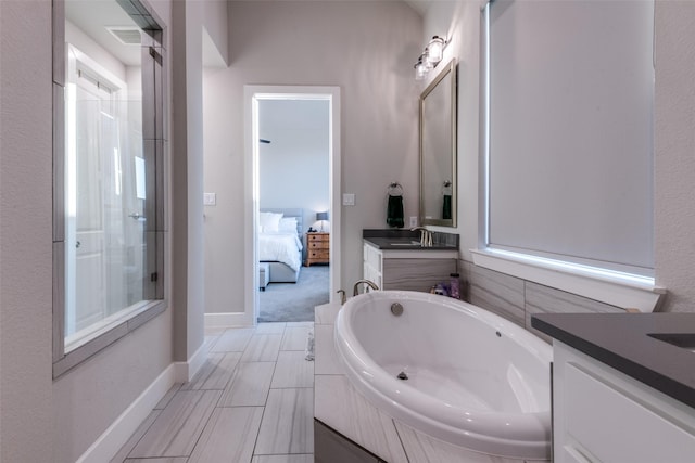 ensuite bathroom with a garden tub, connected bathroom, vanity, and baseboards