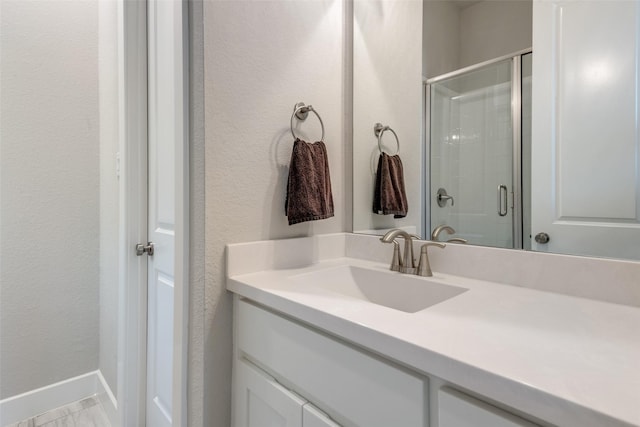 full bathroom featuring baseboards, a textured wall, a shower stall, and vanity