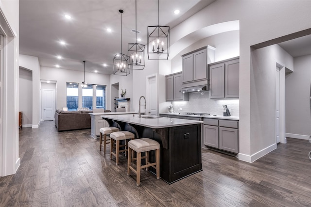 kitchen with dark wood finished floors, gray cabinets, light countertops, backsplash, and a kitchen island with sink