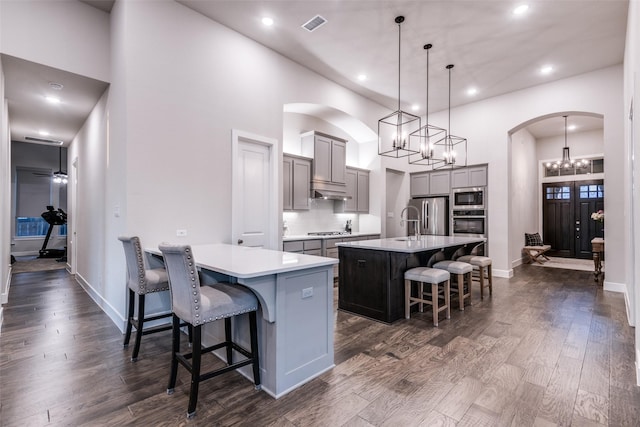 kitchen featuring arched walkways, dark wood-style flooring, stainless steel appliances, gray cabinetry, and a kitchen bar