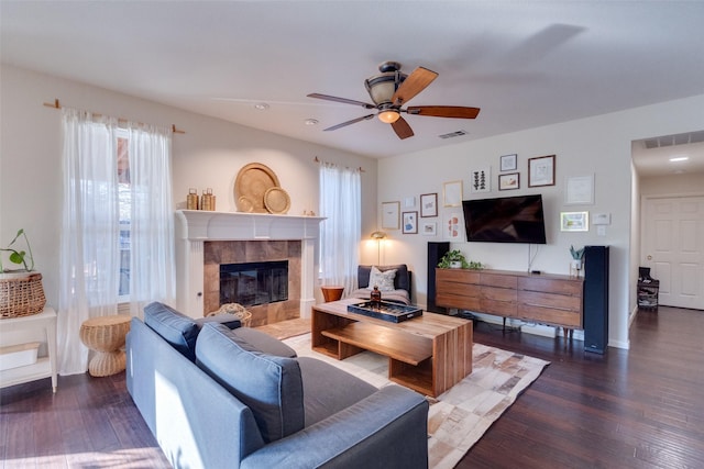 living room featuring a tiled fireplace, ceiling fan, and dark hardwood / wood-style flooring