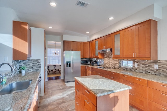 kitchen with a kitchen island, appliances with stainless steel finishes, sink, a chandelier, and light stone countertops