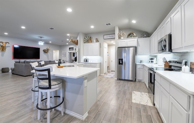 kitchen with appliances with stainless steel finishes, a kitchen bar, a kitchen island with sink, and white cabinets