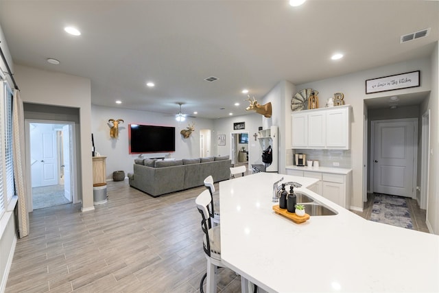 kitchen with sink, light hardwood / wood-style flooring, ceiling fan, backsplash, and white cabinets