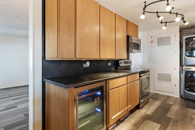 kitchen with appliances with stainless steel finishes, dark hardwood / wood-style floors, stacked washer / dryer, beverage cooler, and backsplash