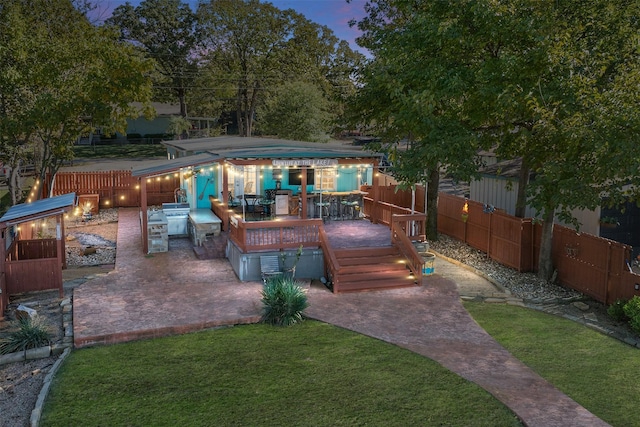 patio terrace at dusk with a wooden deck, an outdoor kitchen, and a lawn