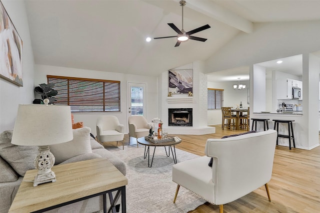 living room with vaulted ceiling with beams, ceiling fan with notable chandelier, a fireplace, and light hardwood / wood-style floors