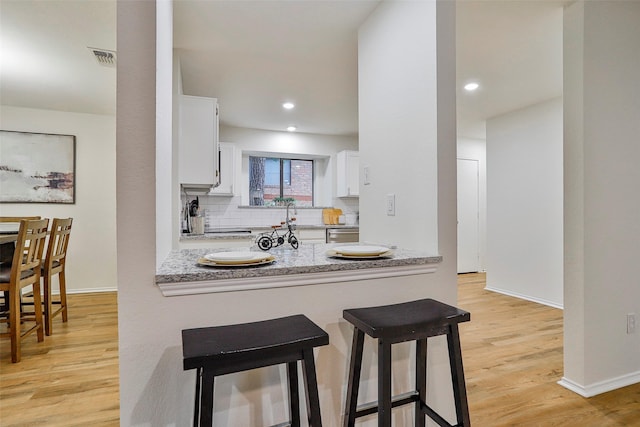 kitchen with dishwasher, white cabinetry, light stone counters, tasteful backsplash, and light wood-type flooring