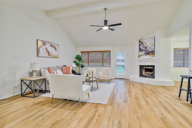 living room with a brick fireplace, lofted ceiling with beams, ceiling fan, and light wood-type flooring