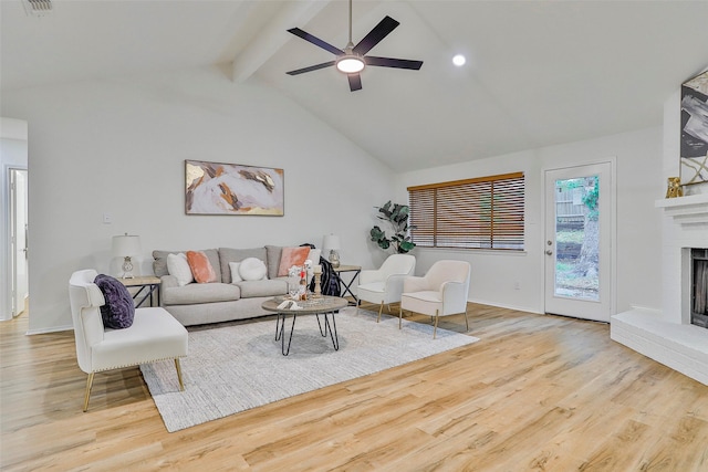 living room featuring high vaulted ceiling, beam ceiling, ceiling fan, a brick fireplace, and light wood-type flooring