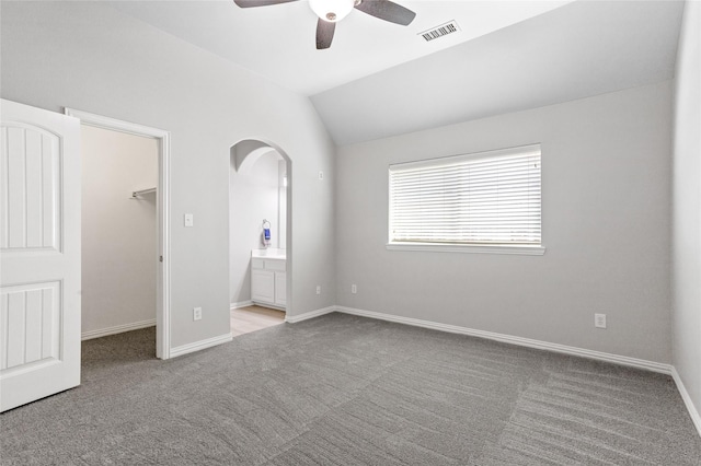 unfurnished bedroom with ensuite bathroom, a walk in closet, vaulted ceiling, light carpet, and ceiling fan