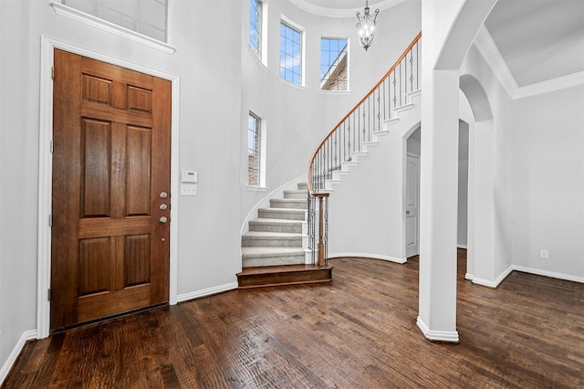 foyer entrance featuring ornamental molding, dark wood-type flooring, an inviting chandelier, and a towering ceiling