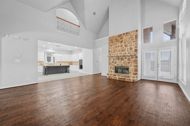 unfurnished living room featuring french doors, high vaulted ceiling, a fireplace, and hardwood / wood-style floors