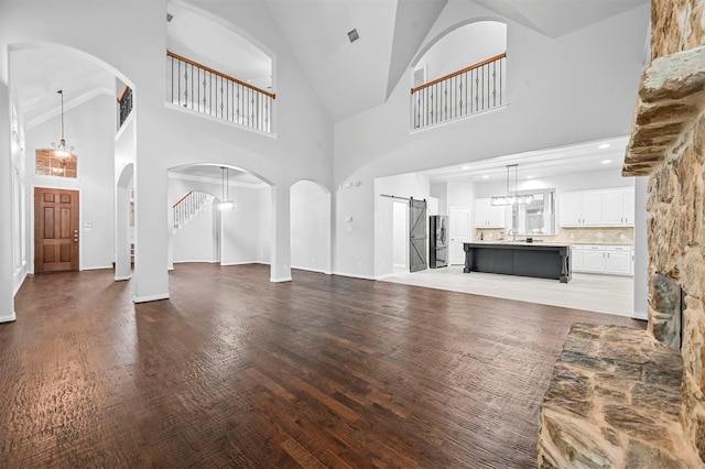 unfurnished living room with a barn door, sink, a notable chandelier, and dark hardwood / wood-style flooring