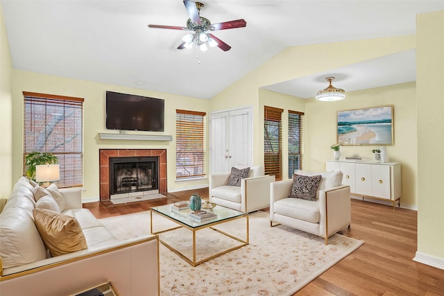 living room with ceiling fan, a tile fireplace, vaulted ceiling, and light hardwood / wood-style flooring