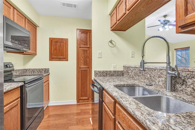 kitchen with sink, ceiling fan, stainless steel appliances, light hardwood / wood-style floors, and light stone countertops