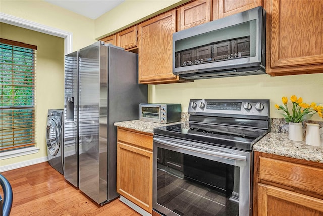 kitchen featuring stainless steel appliances, washer / dryer, light stone counters, and light hardwood / wood-style floors