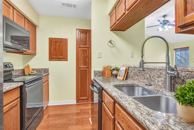 kitchen with sink, ceiling fan, light hardwood / wood-style floors, stainless steel appliances, and light stone countertops