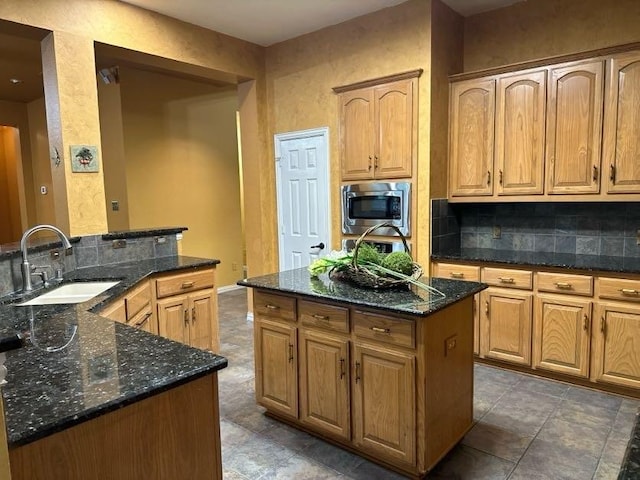 kitchen with stainless steel microwave, sink, dark stone countertops, and a center island with sink