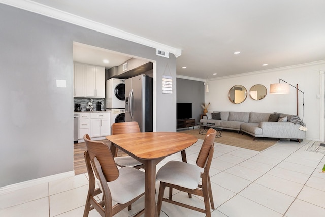 dining space featuring stacked washer / drying machine, crown molding, and light tile patterned flooring