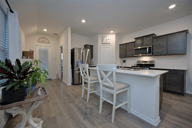 kitchen with stainless steel appliances, a center island with sink, dark brown cabinetry, and light wood-type flooring