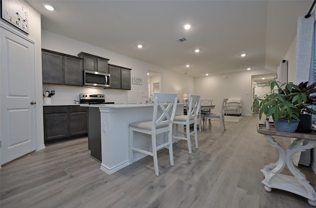 kitchen with stainless steel appliances, a breakfast bar, a center island with sink, and light hardwood / wood-style floors