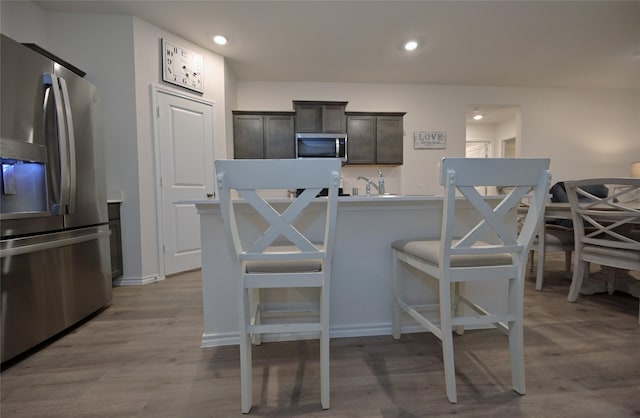 kitchen featuring dark brown cabinetry, a kitchen bar, sink, light hardwood / wood-style flooring, and stainless steel appliances