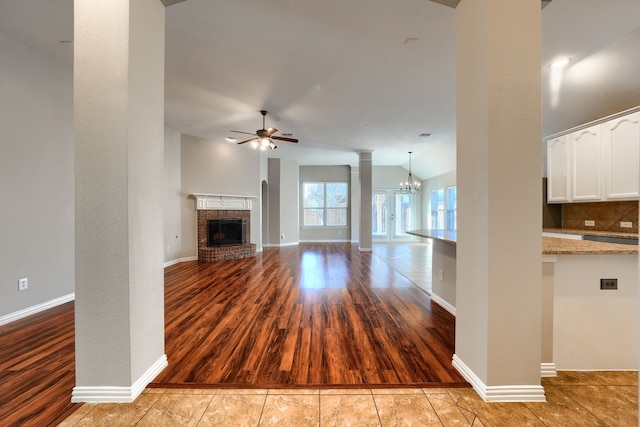 unfurnished living room with lofted ceiling, decorative columns, ceiling fan with notable chandelier, a fireplace, and light hardwood / wood-style floors