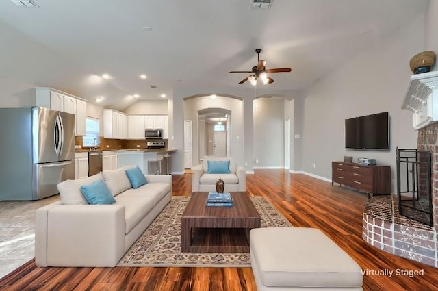 living room featuring lofted ceiling, a brick fireplace, wood-type flooring, and sink