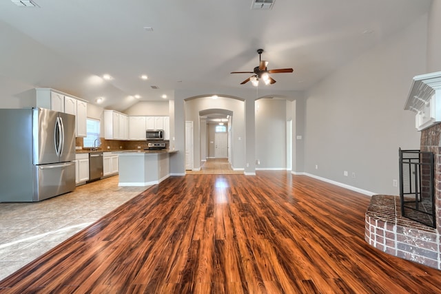 unfurnished living room featuring lofted ceiling, a brick fireplace, light hardwood / wood-style floors, and ceiling fan