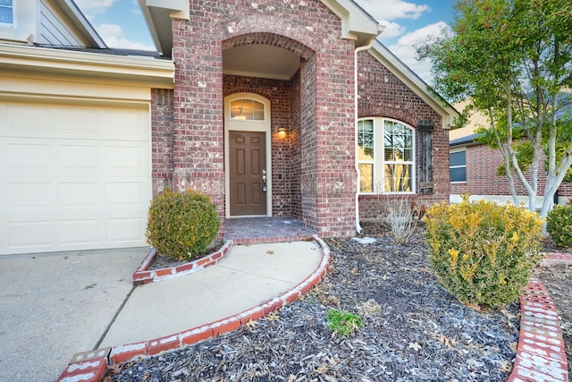 view of exterior entry with an attached garage and brick siding