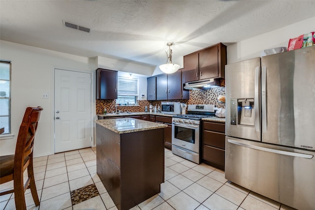 kitchen featuring appliances with stainless steel finishes, hanging light fixtures, a center island, light stone counters, and dark brown cabinetry