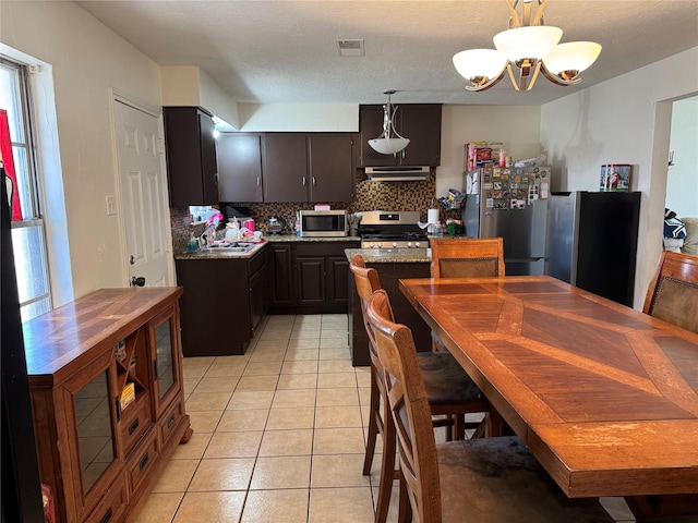 kitchen featuring dark brown cabinetry, decorative light fixtures, light tile patterned floors, appliances with stainless steel finishes, and decorative backsplash