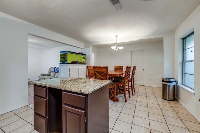 kitchen with pendant lighting, an inviting chandelier, light stone counters, dark brown cabinetry, and light tile patterned flooring