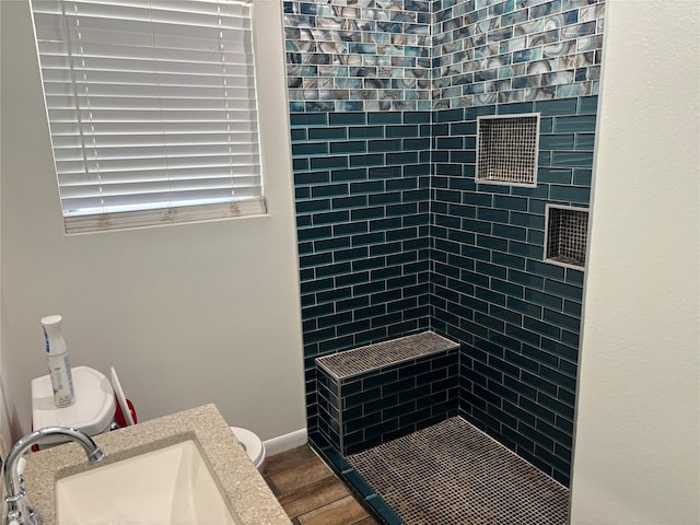 bathroom featuring wood-type flooring, toilet, sink, and a tile shower