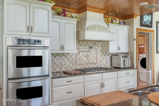 kitchen with backsplash, custom range hood, white cabinets, and appliances with stainless steel finishes