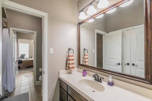 bathroom with tile patterned floors, vanity, a textured wall, and toilet