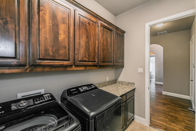 clothes washing area featuring cabinets, washing machine and clothes dryer, and dark hardwood / wood-style floors