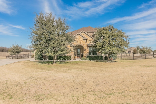 obstructed view of property with stone siding, fence, and a front yard