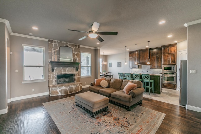 living room featuring a textured ceiling, ornamental molding, dark hardwood / wood-style flooring, ceiling fan, and a fireplace